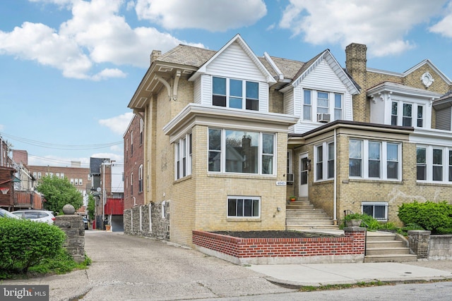 view of property featuring a chimney, cooling unit, and brick siding