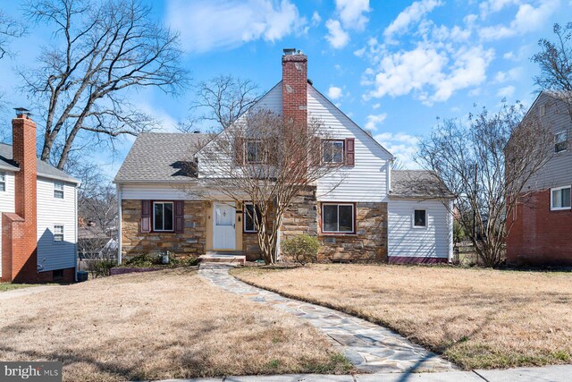 view of front facade featuring a chimney, stone siding, roof with shingles, and a front yard