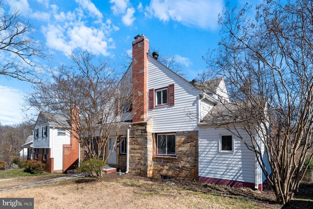 view of side of property featuring a shingled roof, a lawn, stone siding, and a chimney