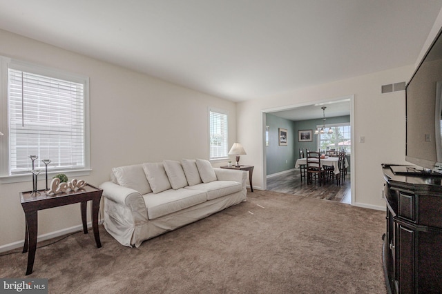 carpeted living room featuring visible vents, baseboards, and a notable chandelier