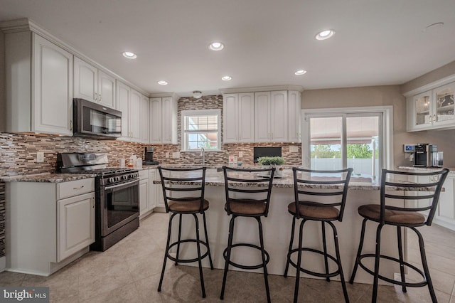 kitchen featuring light stone countertops, a kitchen breakfast bar, white cabinets, appliances with stainless steel finishes, and backsplash