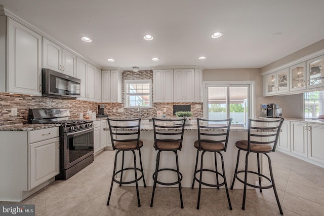 kitchen with a healthy amount of sunlight, appliances with stainless steel finishes, a kitchen breakfast bar, and backsplash