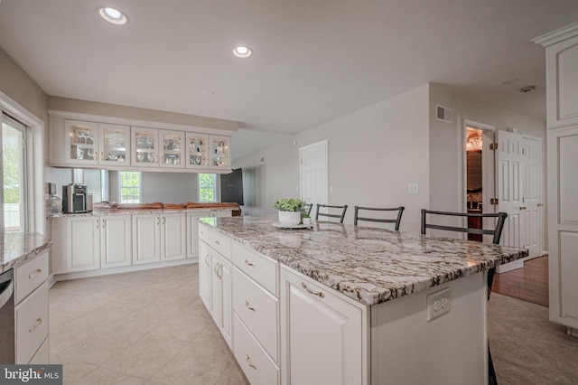 kitchen featuring a breakfast bar area, a kitchen island, visible vents, light stone countertops, and glass insert cabinets