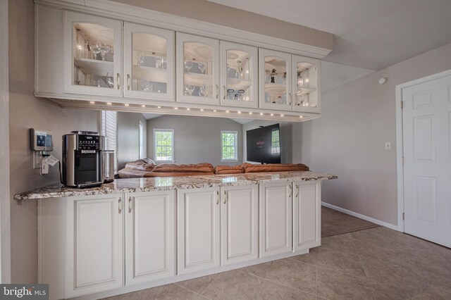 kitchen featuring white cabinetry, light stone countertops, light tile patterned flooring, and glass insert cabinets