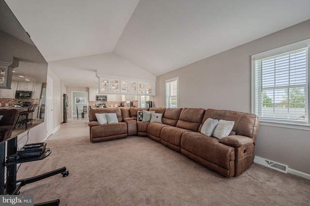living area featuring visible vents, baseboards, vaulted ceiling, and light carpet
