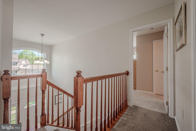 corridor with carpet floors, a chandelier, and an upstairs landing