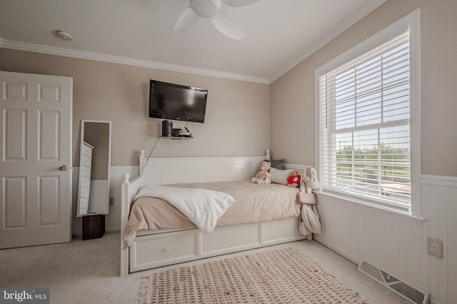 bedroom featuring a ceiling fan, visible vents, a wainscoted wall, ornamental molding, and carpet
