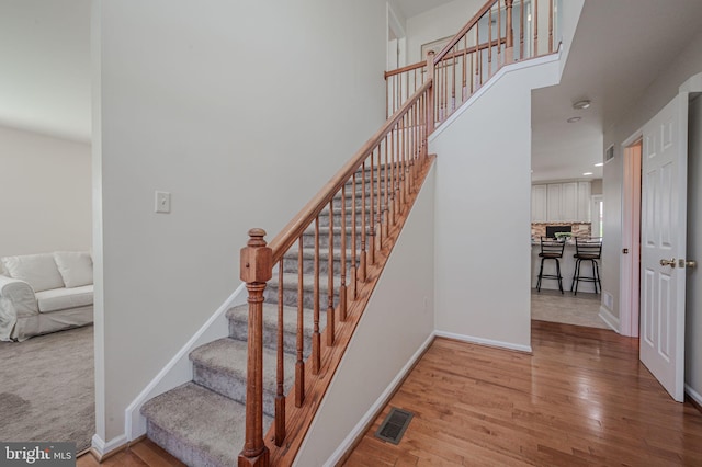 stairs featuring visible vents, baseboards, a towering ceiling, and wood finished floors
