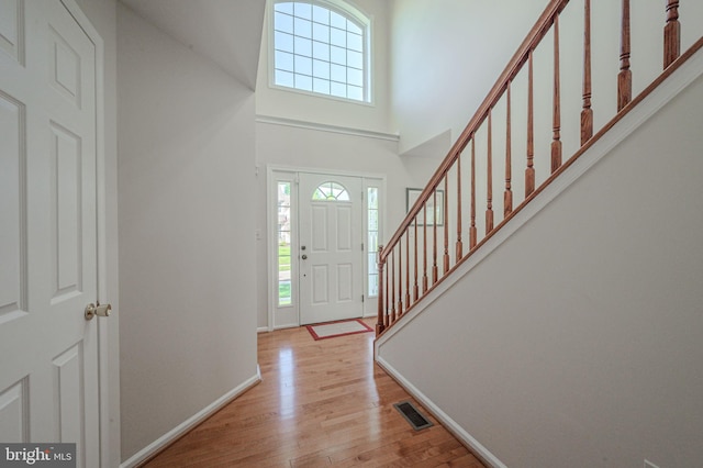 foyer with a towering ceiling, visible vents, stairway, baseboards, and light wood finished floors