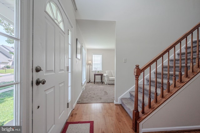 foyer entrance with stairway, baseboards, and light wood finished floors