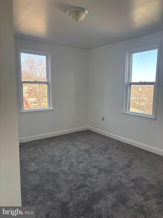 spare room with baseboards and dark colored carpet