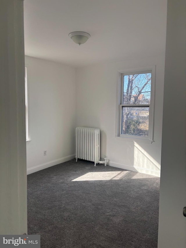 spare room with baseboards, dark colored carpet, and radiator heating unit