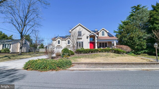 view of front of house with a chimney, solar panels, concrete driveway, and fence