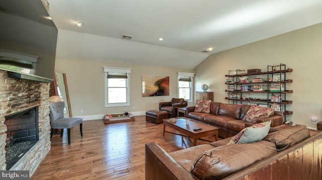 living area featuring visible vents, wood finished floors, a stone fireplace, baseboards, and vaulted ceiling