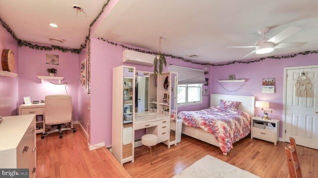 bedroom featuring a baseboard heating unit, an AC wall unit, light wood-style flooring, and visible vents