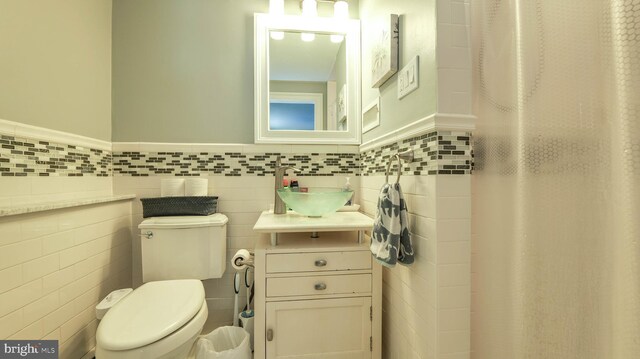 bathroom featuring a wainscoted wall, toilet, tile walls, and vanity