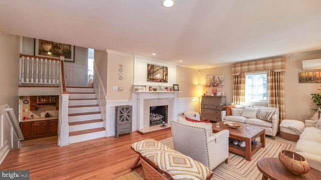 living room with a fireplace with raised hearth, stairway, ornamental molding, light wood-style flooring, and a wall mounted AC