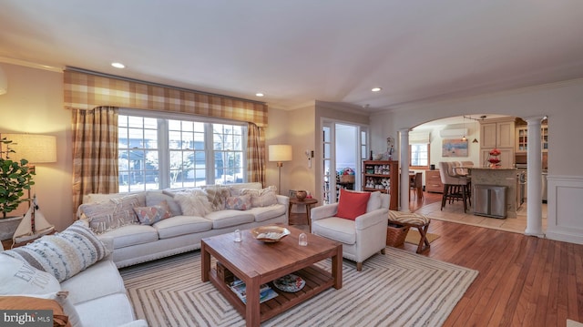 living room with arched walkways, crown molding, light wood-style floors, and decorative columns