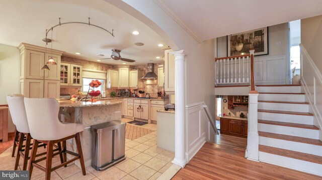 kitchen with a breakfast bar area, arched walkways, ceiling fan, wall chimney range hood, and backsplash