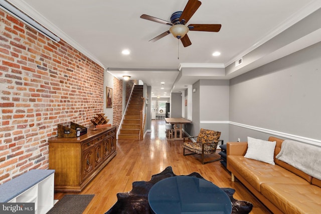 living room with stairway, crown molding, brick wall, ceiling fan, and light wood finished floors