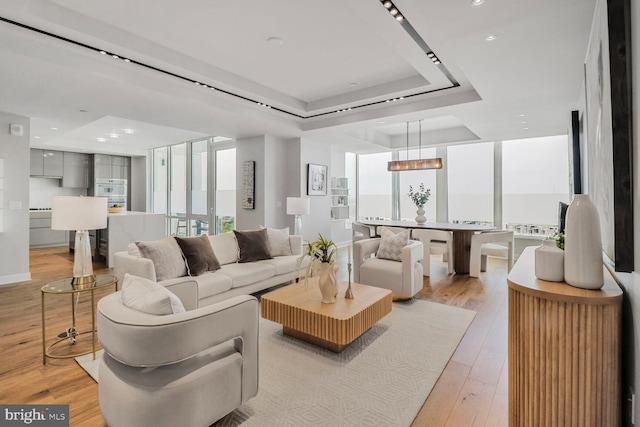 living room with recessed lighting, an inviting chandelier, light wood-type flooring, and a tray ceiling