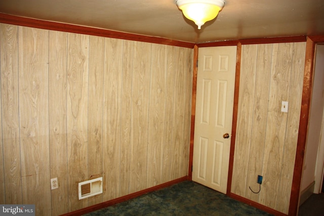 interior space with dark carpet, wooden walls, visible vents, and baseboards