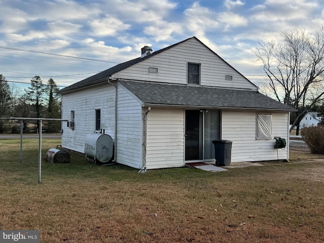 back of property with a lawn, heating fuel, a shingled roof, and fence
