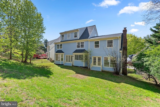 rear view of house featuring french doors, a chimney, fence, entry steps, and a lawn