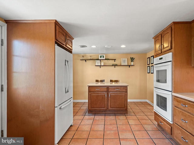 kitchen with white appliances, light tile patterned floors, brown cabinetry, and light countertops