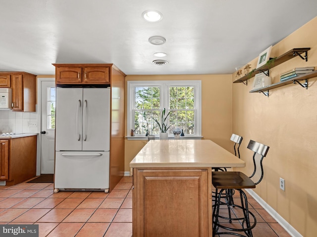 kitchen with a kitchen bar, white appliances, brown cabinetry, light countertops, and light tile patterned floors