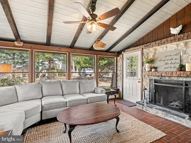 living area featuring vaulted ceiling with beams, a stone fireplace, wooden ceiling, brick floor, and a ceiling fan