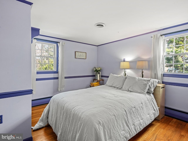 bedroom featuring wood finished floors, visible vents, and baseboard heating