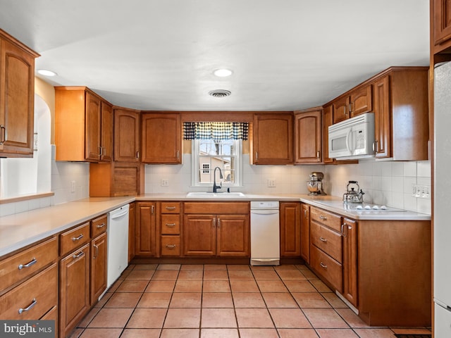 kitchen with visible vents, a sink, white appliances, brown cabinetry, and light tile patterned floors