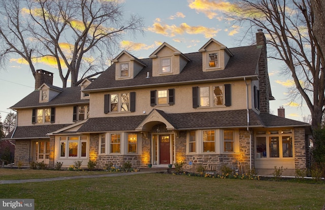 view of front facade with stone siding, a chimney, a front lawn, a shingled roof, and stucco siding