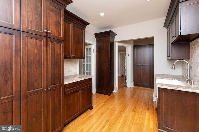 kitchen featuring tasteful backsplash, light wood-style floors, light stone counters, recessed lighting, and a sink