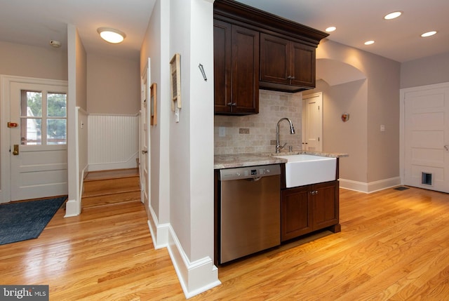 kitchen featuring stainless steel dishwasher, dark brown cabinets, a sink, backsplash, and light wood finished floors