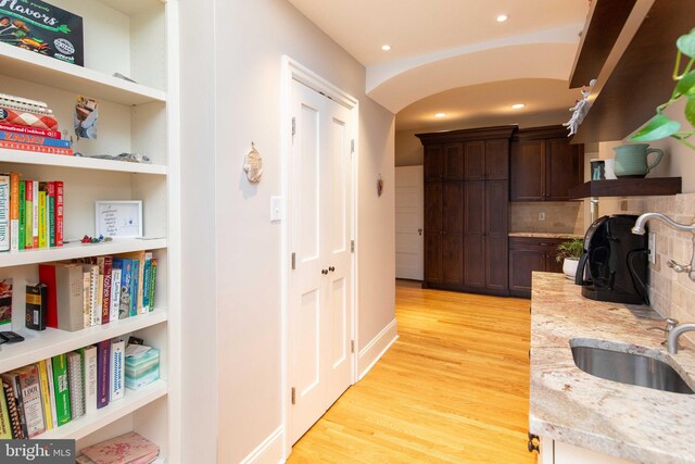 hallway with a sink, light wood finished floors, recessed lighting, and arched walkways