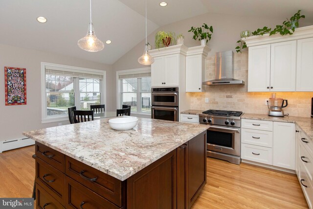 kitchen featuring stainless steel appliances, wall chimney range hood, vaulted ceiling, white cabinets, and backsplash