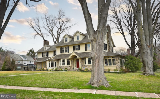 view of front of home featuring stone siding, stucco siding, a front yard, a chimney, and a shingled roof