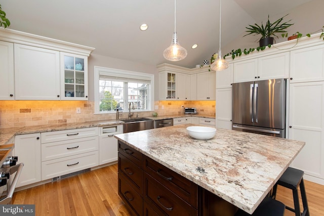 kitchen featuring stainless steel appliances, a sink, a kitchen bar, decorative backsplash, and decorative light fixtures