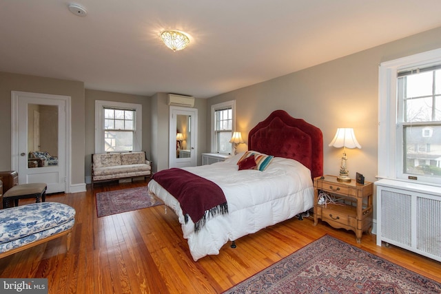 bedroom with radiator, a wall mounted AC, multiple windows, and wood-type flooring