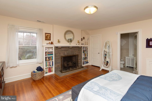 bedroom with radiator, baseboards, a fireplace with raised hearth, wood finished floors, and ensuite bathroom