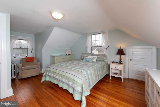 bedroom featuring hardwood / wood-style flooring, multiple windows, vaulted ceiling, and radiator heating unit