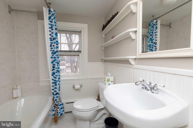 bathroom featuring wainscoting, a sink, toilet, tile patterned flooring, and shower / bath combination with curtain
