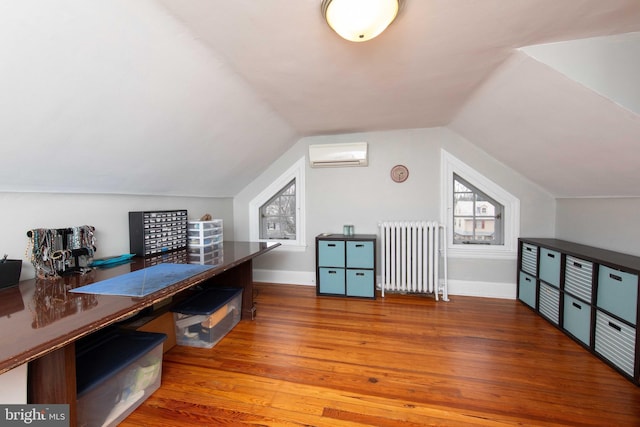home office featuring radiator, a wall mounted AC, wood finished floors, baseboards, and vaulted ceiling
