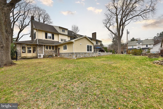 back of house featuring a chimney, stucco siding, stone siding, and a yard