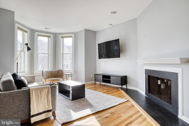 living area with visible vents, baseboards, a glass covered fireplace, and wood finished floors