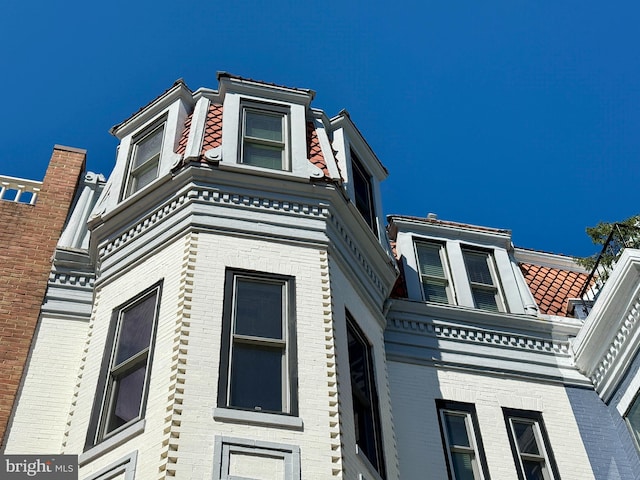 view of home's exterior featuring brick siding, a tiled roof, and mansard roof