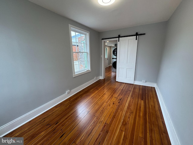 unfurnished bedroom featuring stacked washer / dryer, dark wood-style flooring, baseboards, and a barn door
