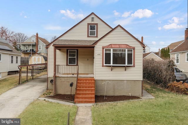 bungalow featuring driveway, a shed, covered porch, an outdoor structure, and a front lawn